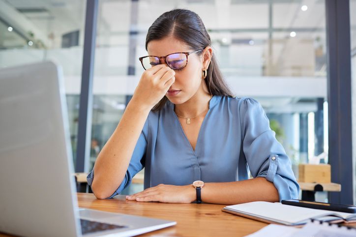 Gestresste Frau im Büro, überfordert mit der Arbeitsbelastung am Schreibtisch mit Laptop.